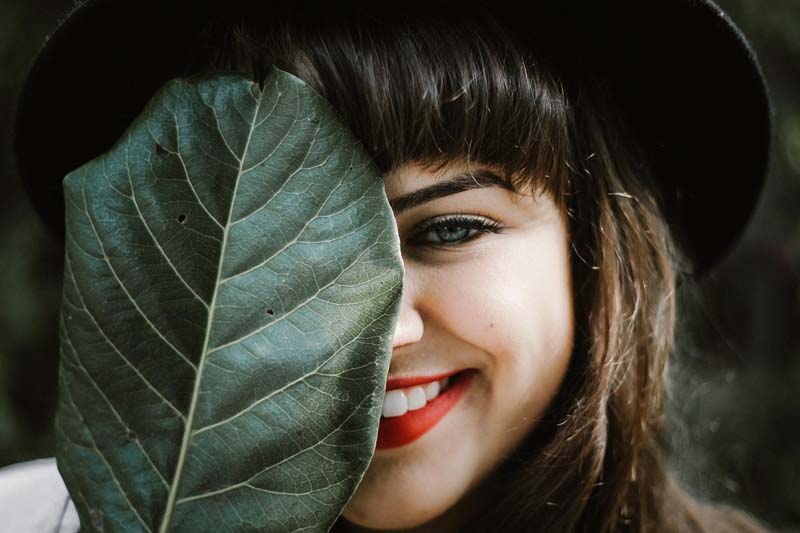 girl smiling, hiding behind a leaf