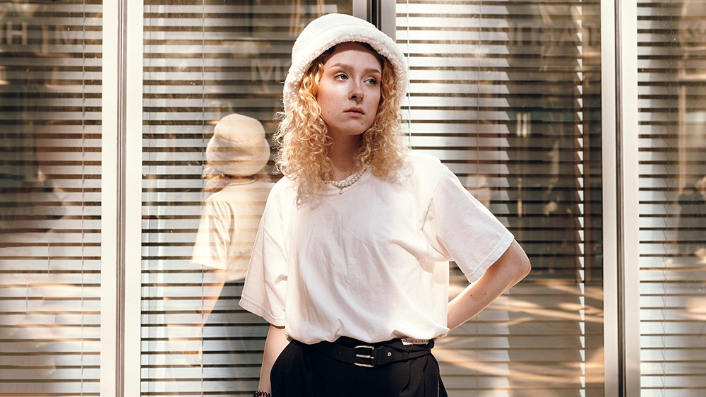 Young woman in a minimalist white tee and bucket hat styled with black belted trousers.