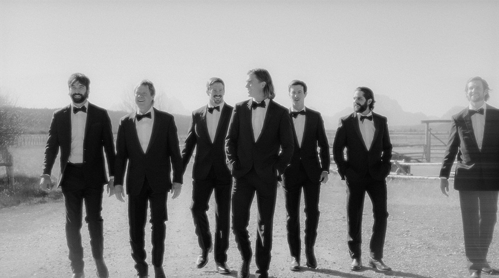 a group of men in tuxedos walking down a road