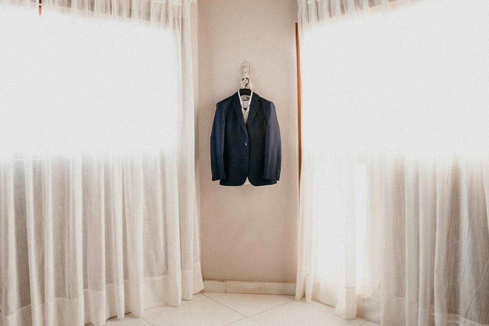 A navy blazer airing on a hanger between bright curtained windows